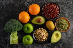 Broccoli, apple, orange, kiwi, avocado and beans on a black cement floor background photo