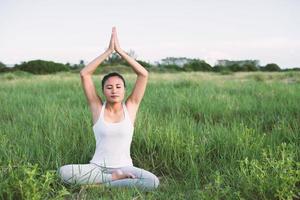 Mujer joven en pose de yoga practicando meditación en los prados