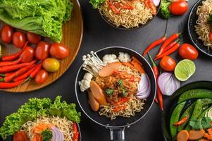 Noodles in a frying pan with ingredients on black cement background photo