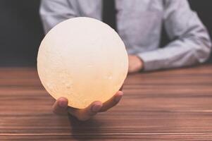 Person holding a moon lamp at a desk photo