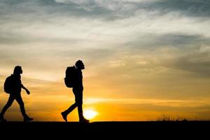 siluetas de dos excursionistas con mochilas disfrutando de la puesta de sol foto