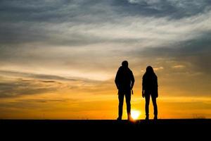 Silhouettes of two hikers with backpacks enjoying the sunset photo