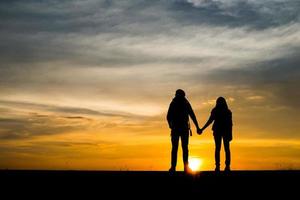 Silhouettes of two hikers with backpacks enjoying the sunset photo