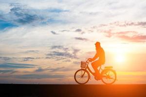 Young man rides a bicycle on sunset background photo