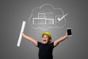 Young boy wearing a yellow engineer hat and house plan ideas on a blackboard photo