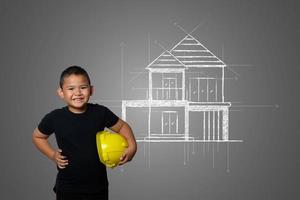 Young boy wearing a yellow engineer hat and house plan ideas on a blackboard photo