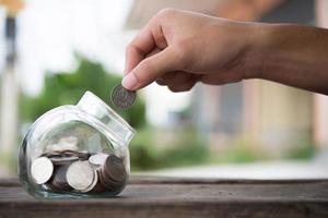 manos poniendo dinero en una botella por dinero en efectivo en el futuro foto