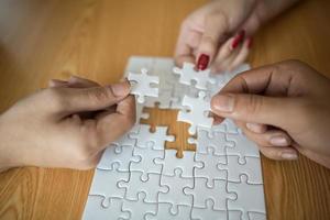 Hands connecting puzzle piece together on wooden table photo