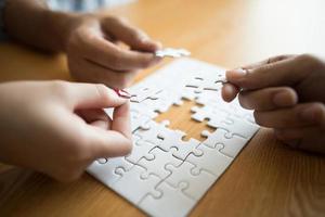 Hands connecting puzzle piece together on wooden table photo