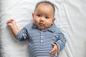 Baby lying face up on a white bed and looking at camera photo