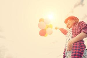 Young hipster woman holding balloons below the sky photo