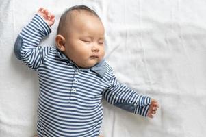 A baby boy in a striped shirt sleeping in bed photo