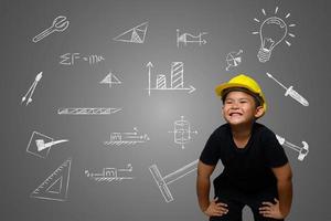 un niño con un sombrero de ingeniero amarillo y un plano de la casa en la pizarra foto