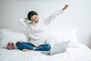 Young woman stretching on bed with laptop photo