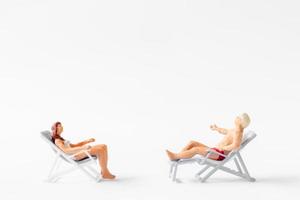 Miniature people sunbathing on deck chairs on white background