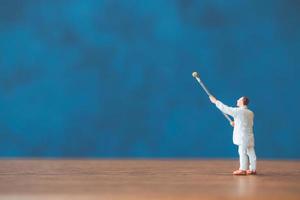 Miniature person holding a brush in front of blue wall background photo