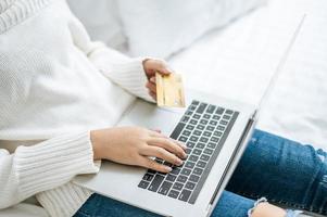 mujer joven de compras en la computadora portátil y sosteniendo una tarjeta de crédito