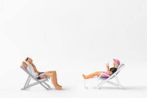 Miniature people sunbathing on deck chairs on white background photo