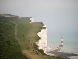 faro junto al acantilado con grupos de personas caminando foto