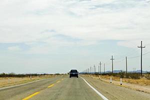 Black SUV on empty road under cloudy blue sky photo