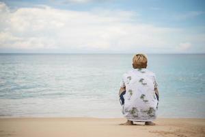 Hombre joven inconformista relajante sentado en la playa del mar foto