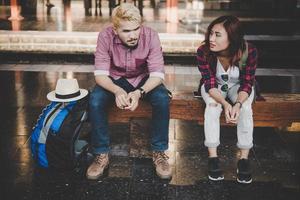 Pareja joven inconformista sentado en un banco de madera en la estación de tren foto