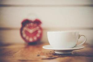 Red alarm clock with coffee on wooden table photo