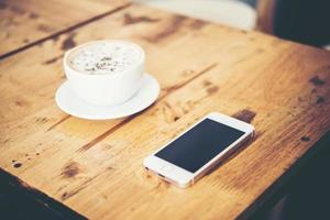 una taza de café y un teléfono inteligente en la mesa de madera en el café