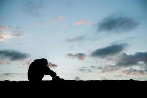 Silhouette of sad woman head on knees at sunset photo