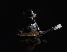 joven guitarrista hipster sobre fondo oscuro foto