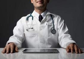 Male medical doctor with a tablet computer sitting isolated at desk photo