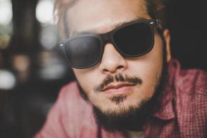 Young hipster man wearing sunglasses sitting at a bar table in a cafe photo