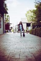 Retrato de mujer joven inconformista con estilo caminando por la calle urbana, sonriendo disfrutar los fines de semana. vintage de hipster adolescente con bolso en mano. foto