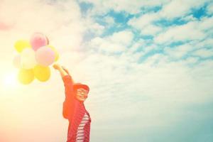 Hermosa joven disfrutando de globos multicolores en el cielo brillante foto