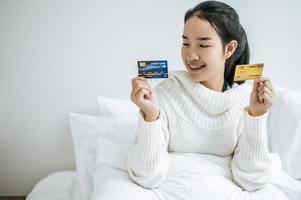 Mujer joven con una tarjeta de crédito sonriendo en la cama