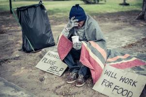 Hombre sin hogar envuelto en tela y comiendo fideos foto