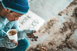 Beggar under the bridge with a cup containing coins and instant noodles photo