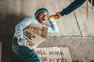 Beggar under the bridge with cardboard help signs accepting bread photo