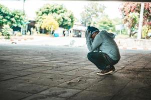 Homeless man sits under the bridge with both hands holding head photo