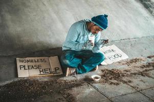 Beggar under the bridge with a cup containing coins and instant noodles photo