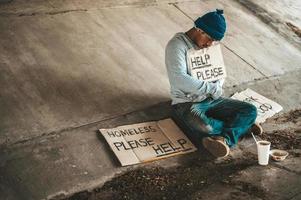 mendigo sentado debajo de un paso elevado con carteles de ayuda foto