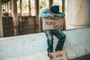 Mendigo se sienta en una barrera de la carretera con personas sin hogar, ayude a firmar foto