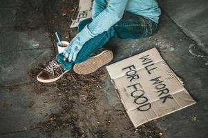 Beggar under the bridge with a cup of instant noodles and a help sign photo