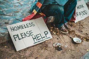 un hombre se sienta mendigando con personas sin hogar por favor mensaje de ayuda foto