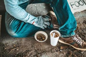 mendigo debajo del puente con una taza de fideos instantáneos y un cartel de ayuda foto