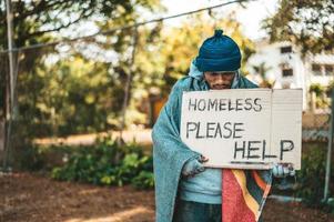 Beggar stands on the street with please help sign photo