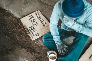 Beggar under the bridge with a cup of instant noodles and a help sign photo