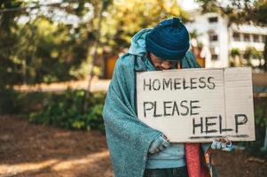 Beggar stands on the street with please help sign photo