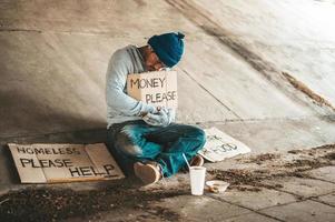 Beggar sitting under the overpass with a please help sign photo