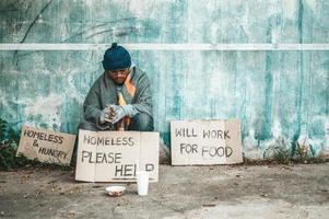 Man sits beside the street with a homeless message photo